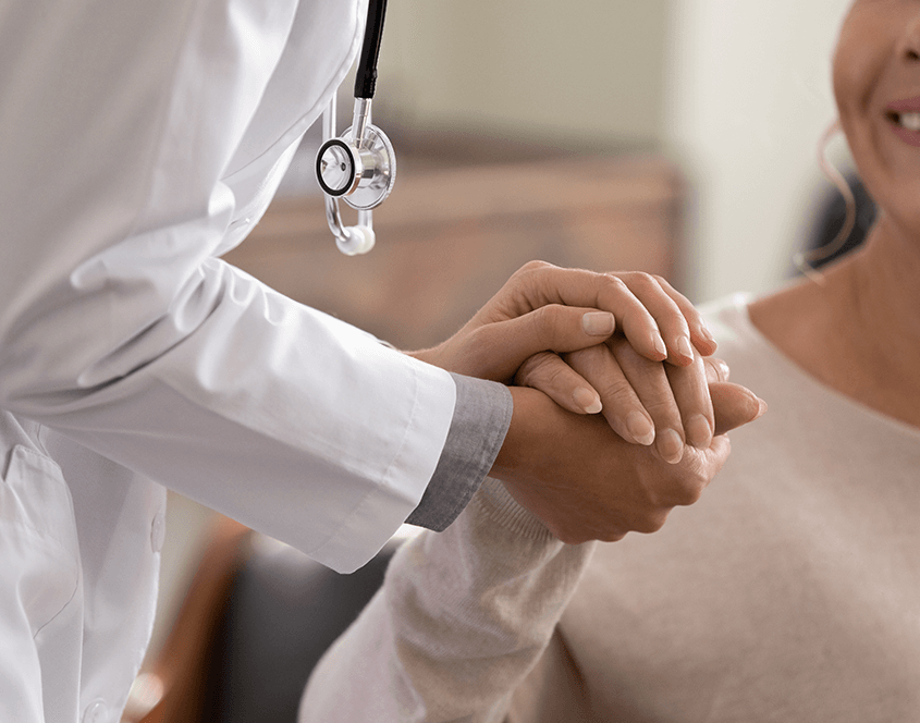 Arzt hält Hand von Patientin, diese lächelt zufrieden.